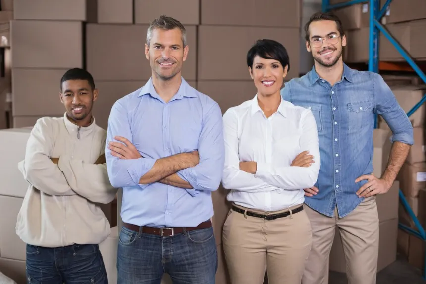 Warehouse Team with Arms Crossed Smiling at Camera in Storage Hub Four warehouse workers standing with arms crossed and smiling in front of stacked boxes in bright storage area business directory